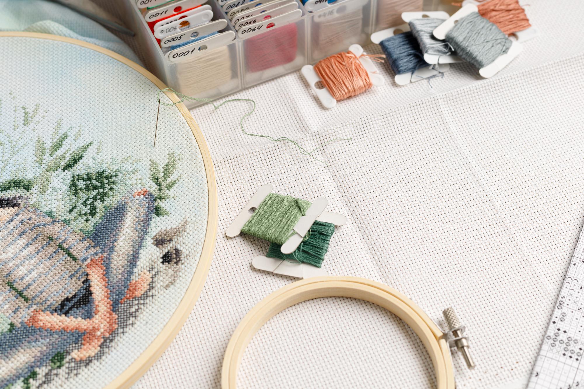 Hand aligning fabric on an embroidery frame beside laptop